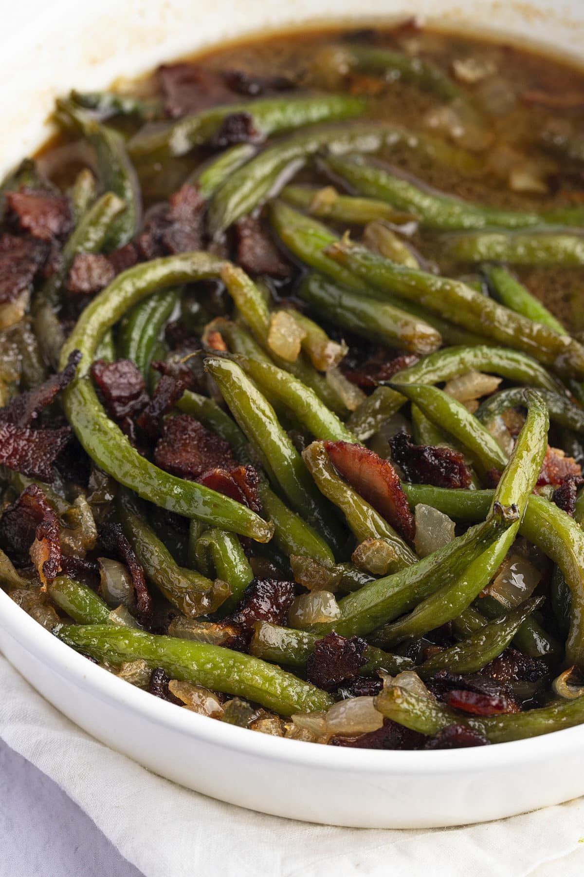 Close up of green beans with sauce, onions and bacon.