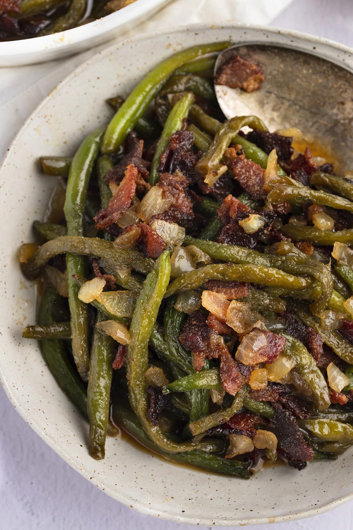 A spoon in a bowl of baked green beans, bacon and onions.