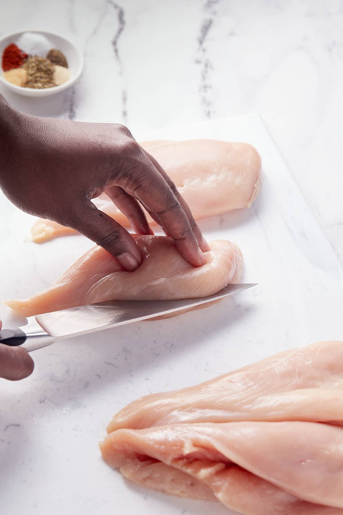 Cutting the chicken breasts in half.