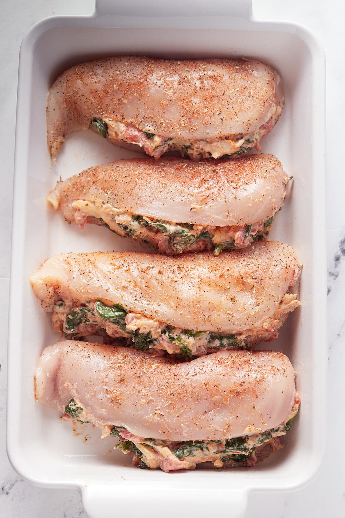Four chicken breasts stuffed with cream cheese and spinach in a white baking dish.