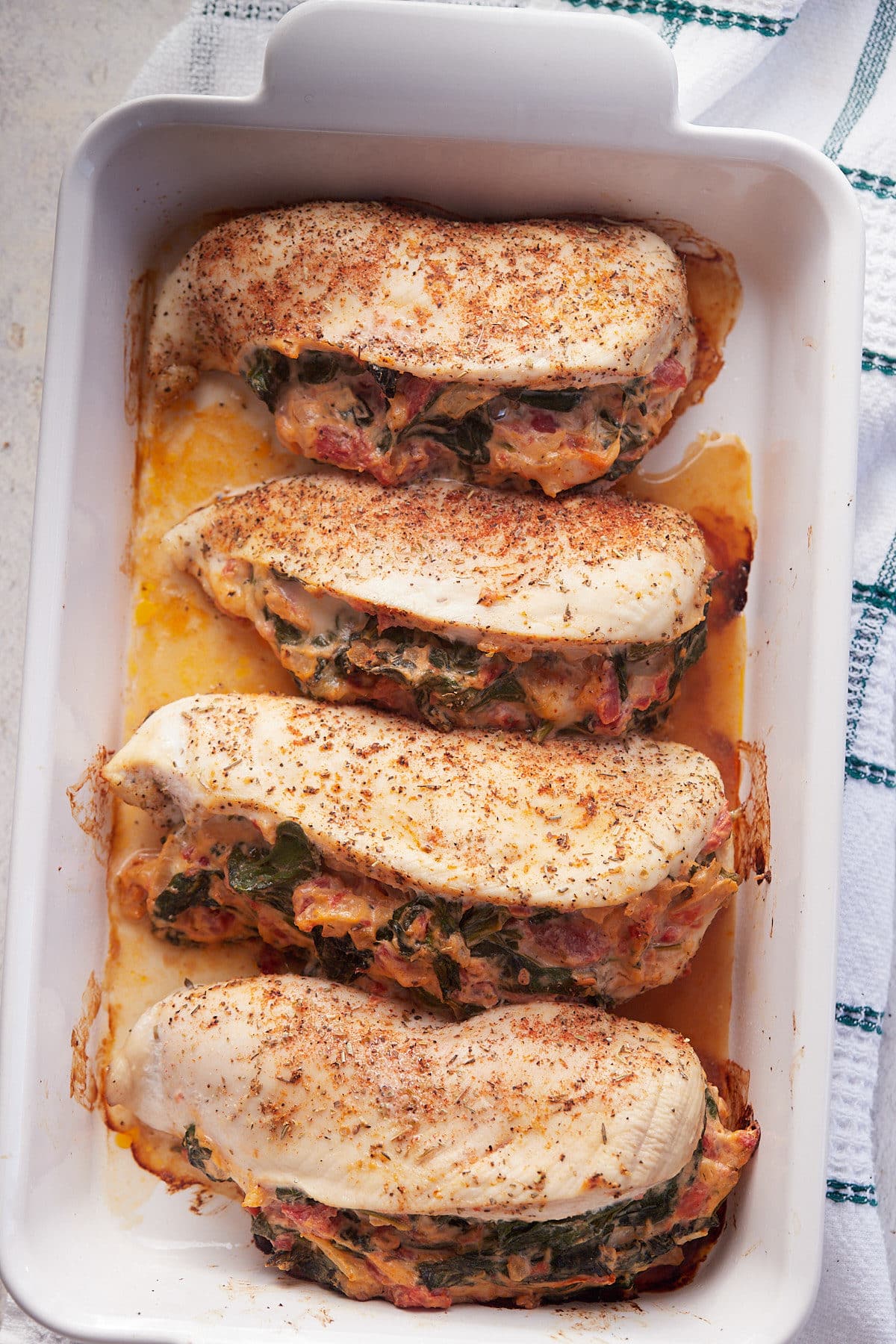 Four baked spinach stuffed chicken breasts in a white baking dish.