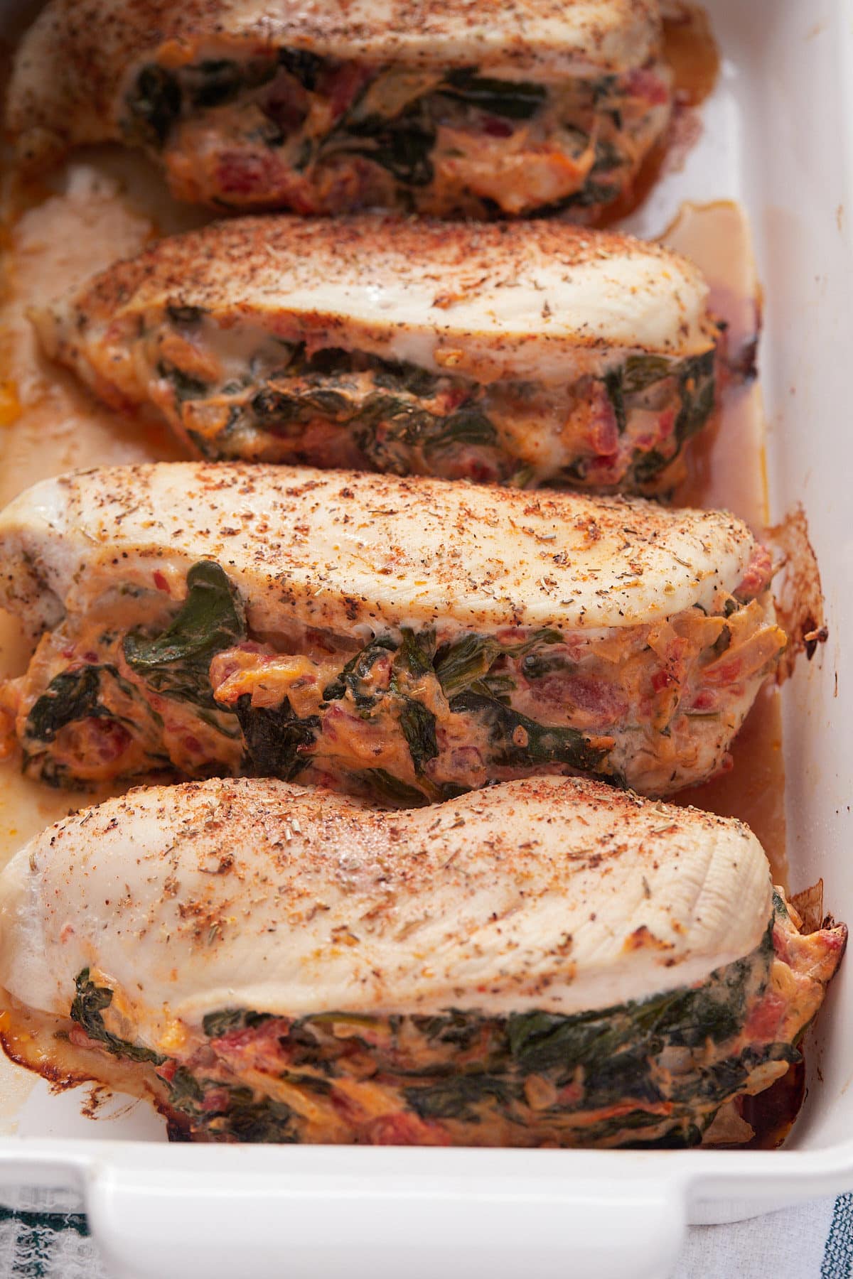 Four baked chicken breasts stuffed with spinach in a baking dish.