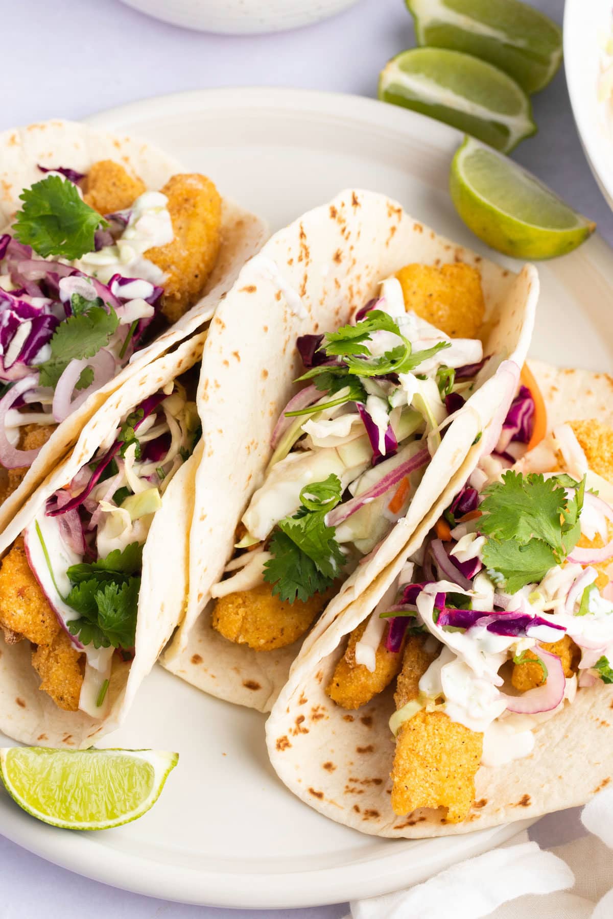 Four air fryer fish tacos served on a plate with fresh cilantro and lime wedges.