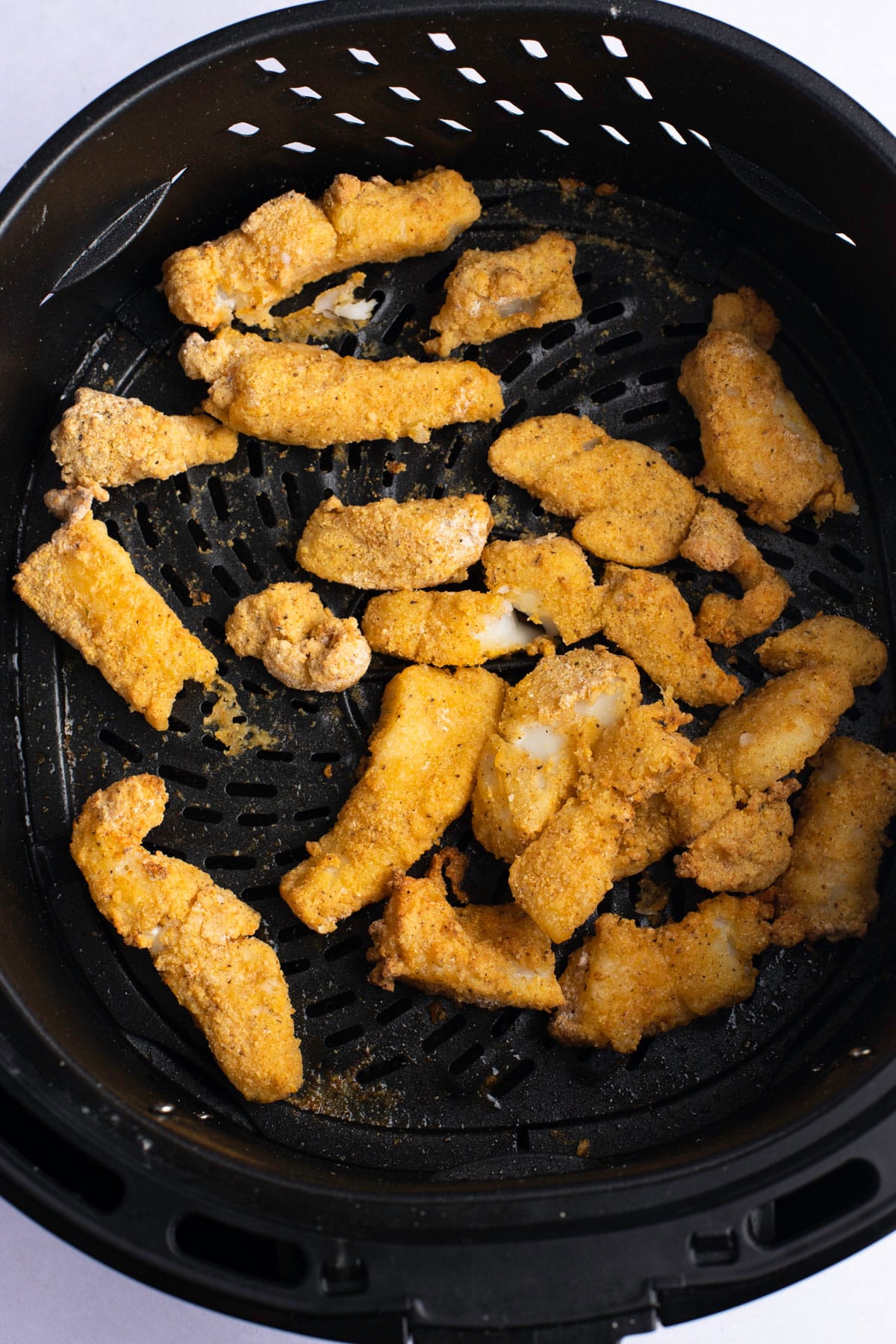 Fried fish strips in an air fryer basket.