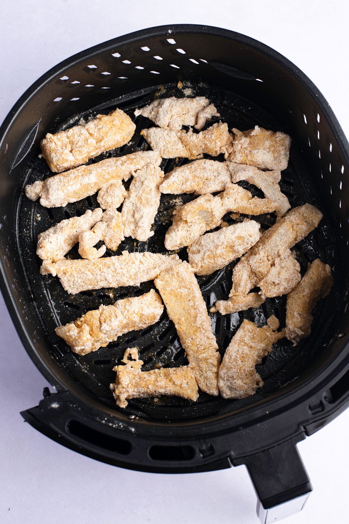 Breaded fish in the air fryer basket before being cooked.