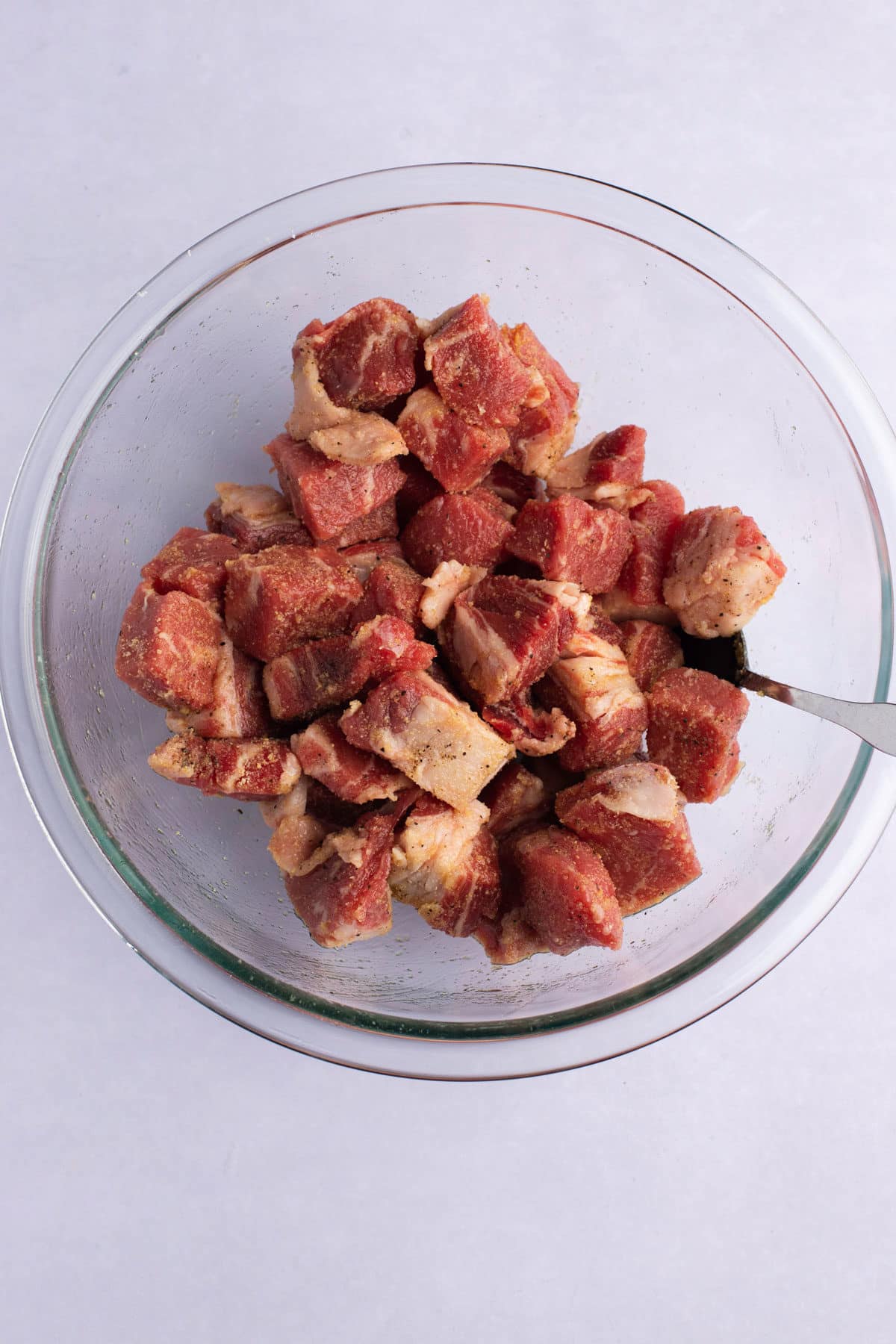 Cubes of raw steak in a bowl with oil and seasonings.