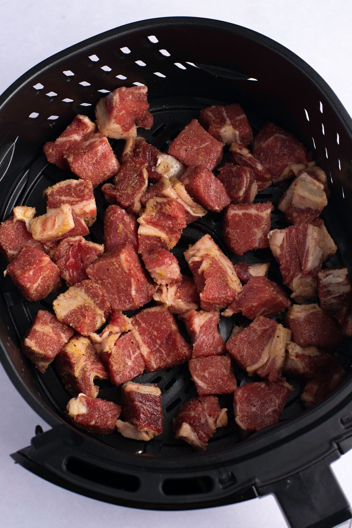 Seasoned steak in an air fryer basket.