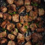 Cooked steak bites in the air fryer basket.