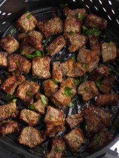 Cooked steak bites in the air fryer basket.