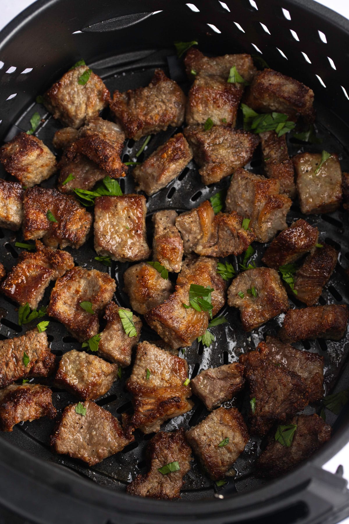 Cooked steak bites in the air fryer basket.