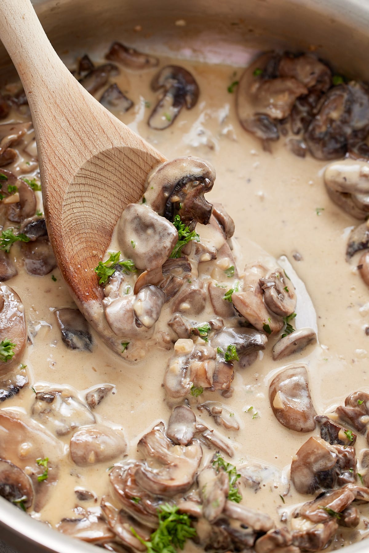 A wooden spoon stirring the mushroom sauce.