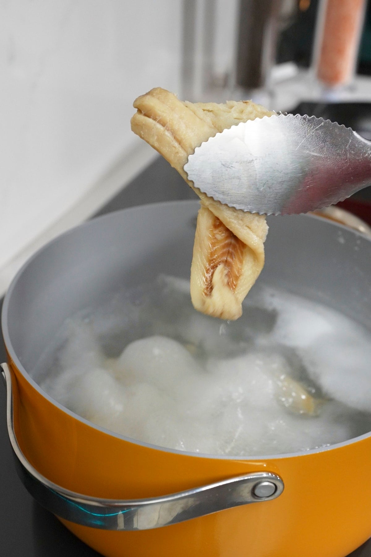 tongs lifting codfish out of boiling water in pot