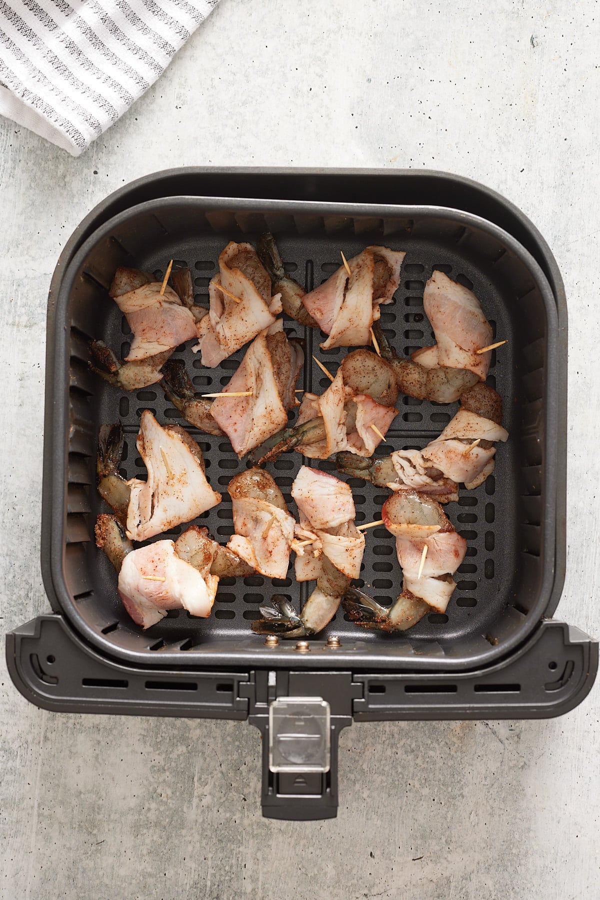 raw shrimp wrapped in raw bacon inside air fryer basket