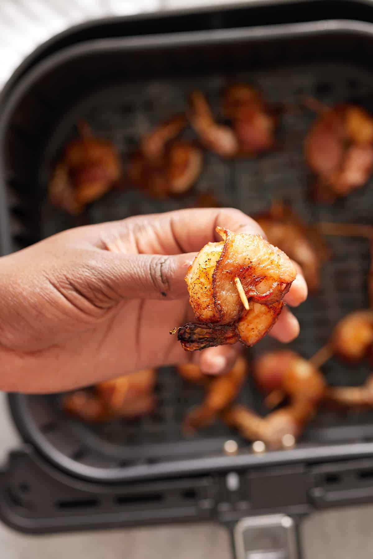 hand holding up bacon wrapped shrimp over air fryer