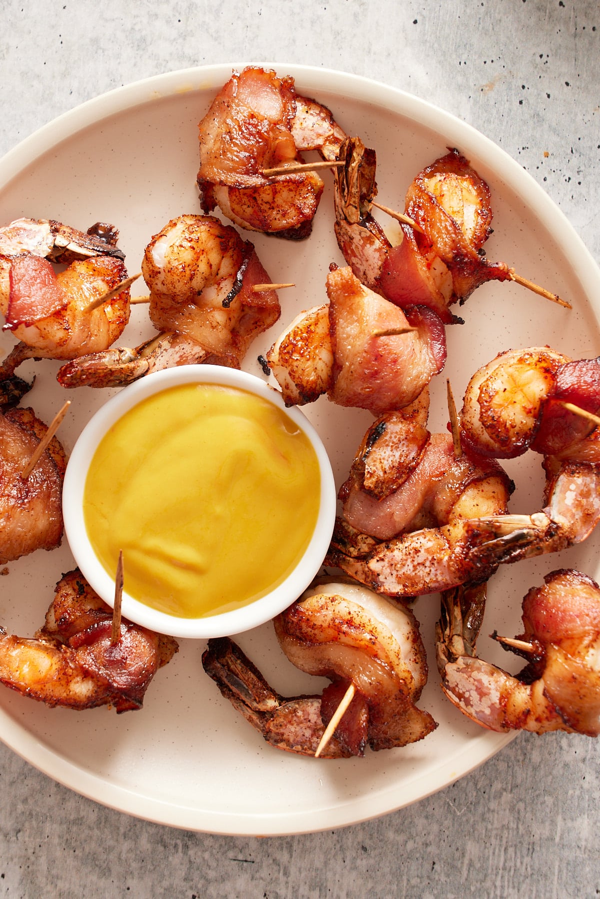 bacon wrapped shrimp on white plate with a dipping sauce