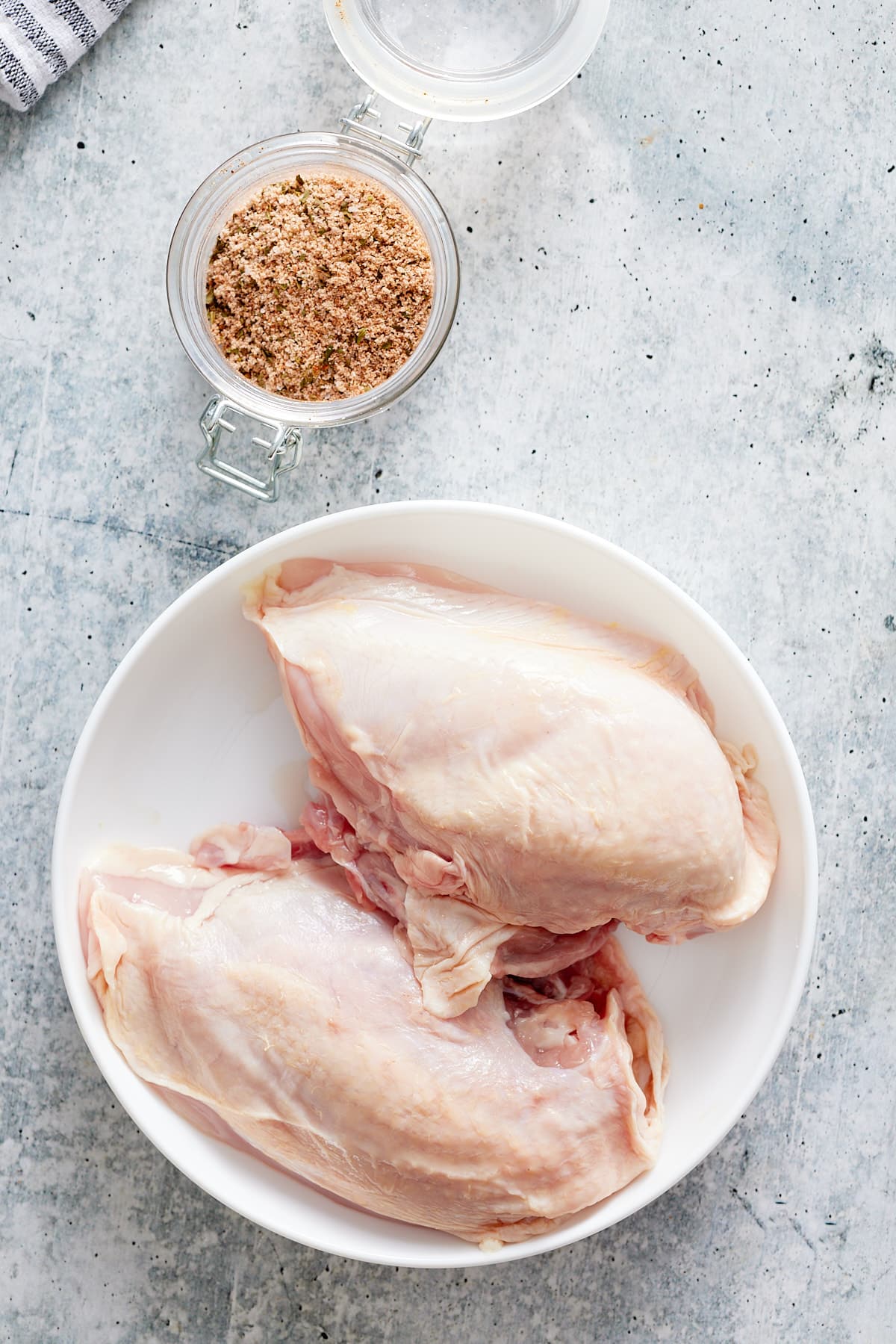 air fryer bone in chicken breasts on white plate with seasoning on sides