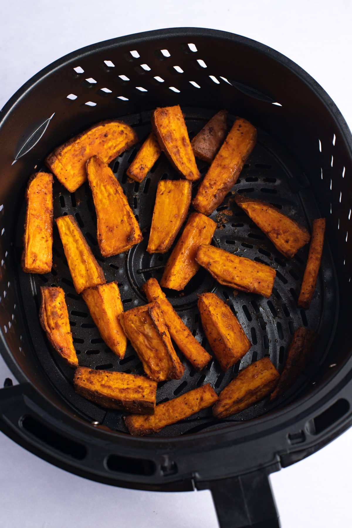 Cooked sweet potato wedges in an air fryer basket.