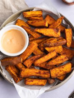 Air fryer sweet potato wedges on a plate with a dip.