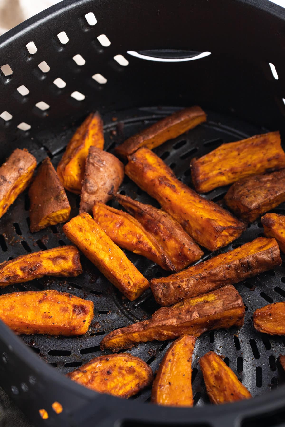 Close up of sweet potato wedges in an air fryer basket.