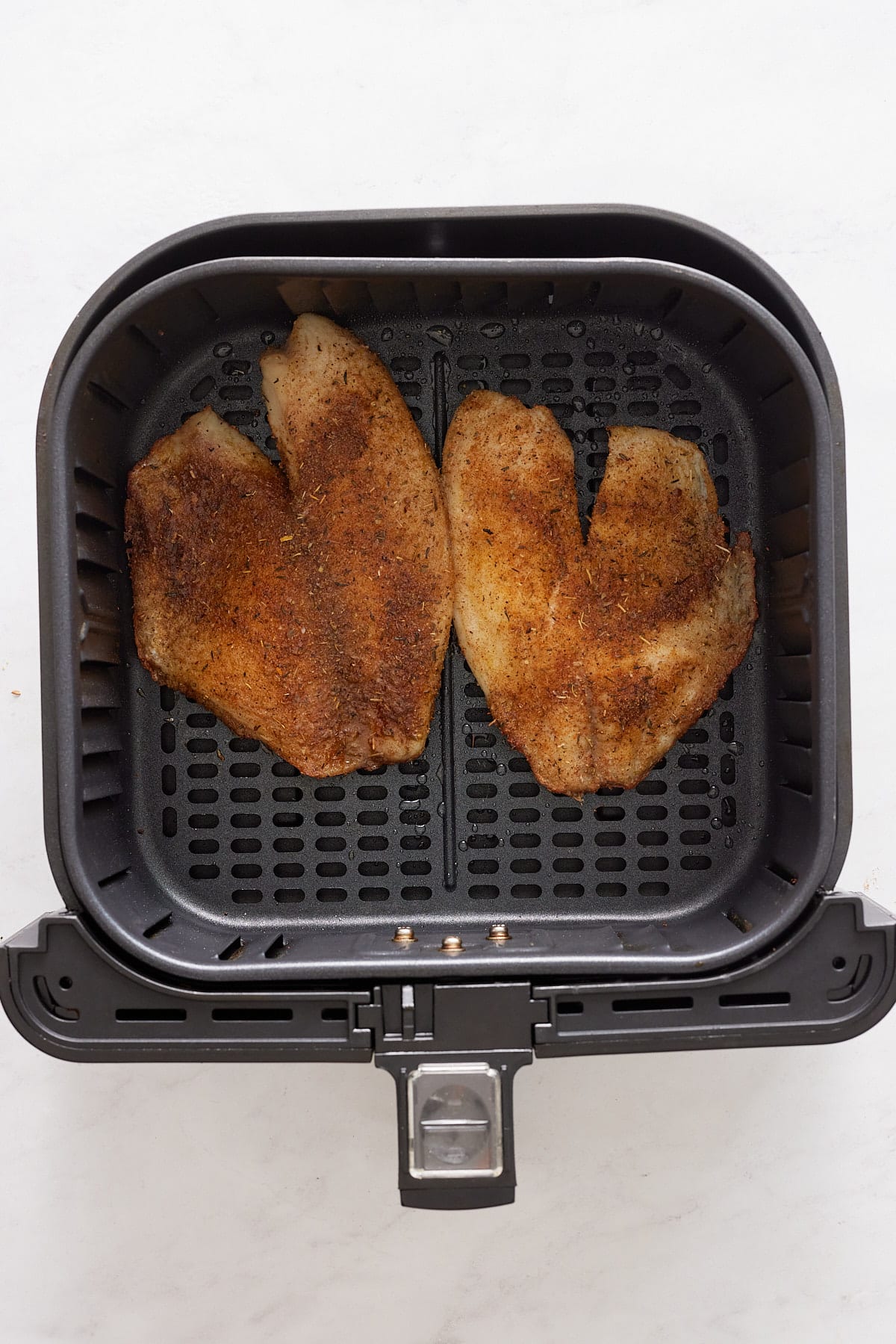 Cooked tilapia filets in the air fryer basket.