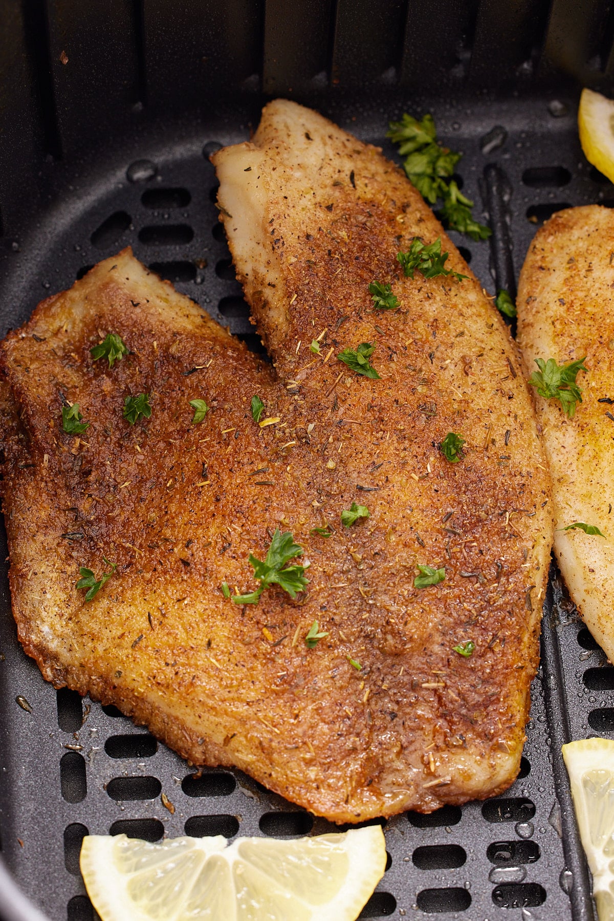 A tilapia fillet in an air fryer basket garnished with fresh parsley.