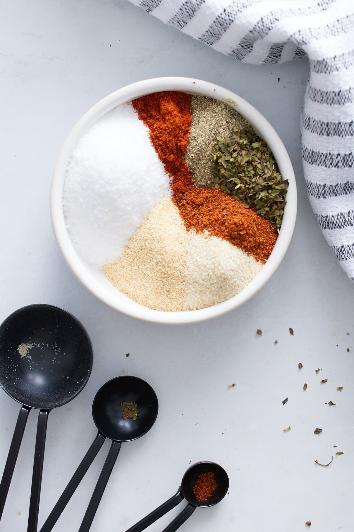 seasonings in white bowl with measuring spoons next to it
