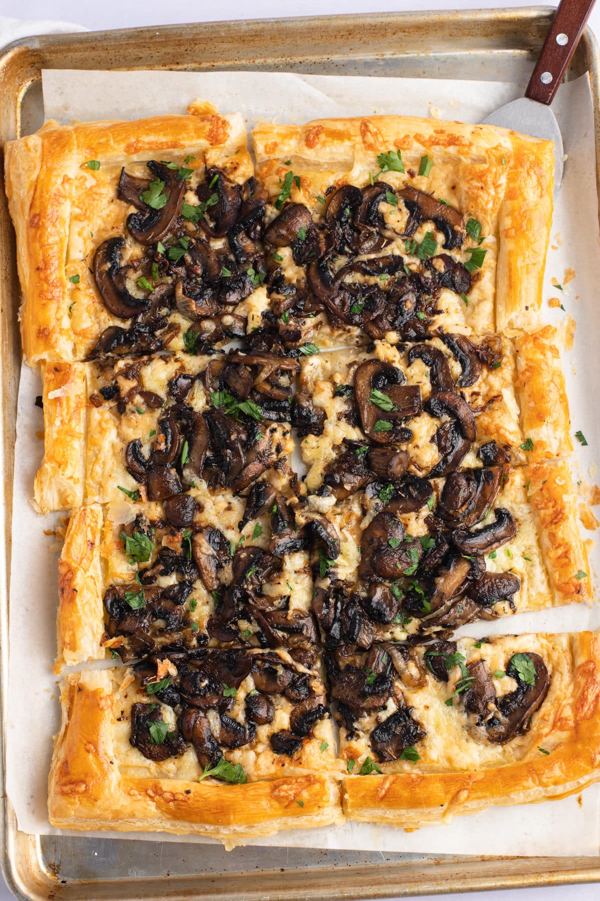 A mushroom tart cut into pieces and garnished with fresh parsley.