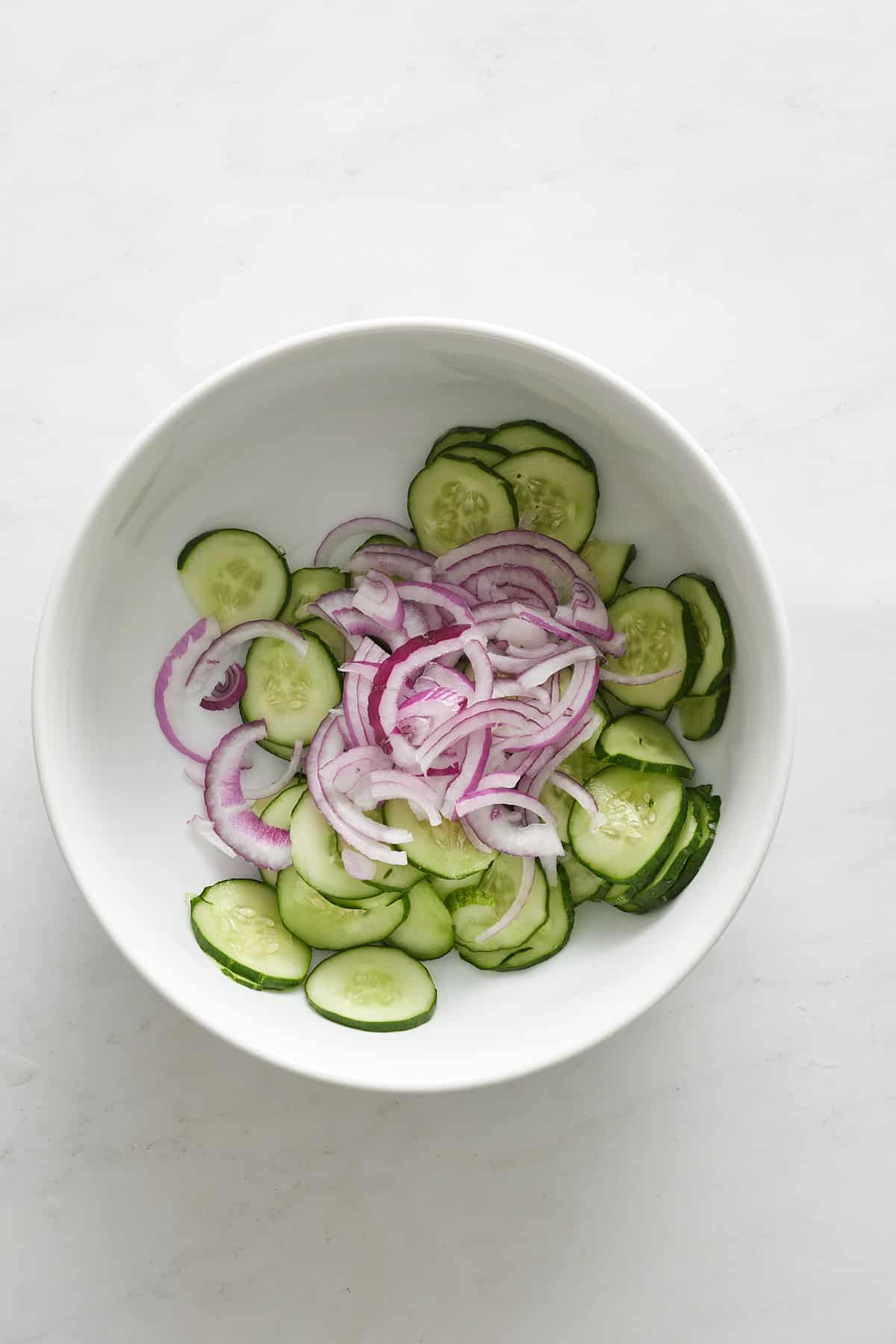 Sliced red onion and cucumbers in a bowl.