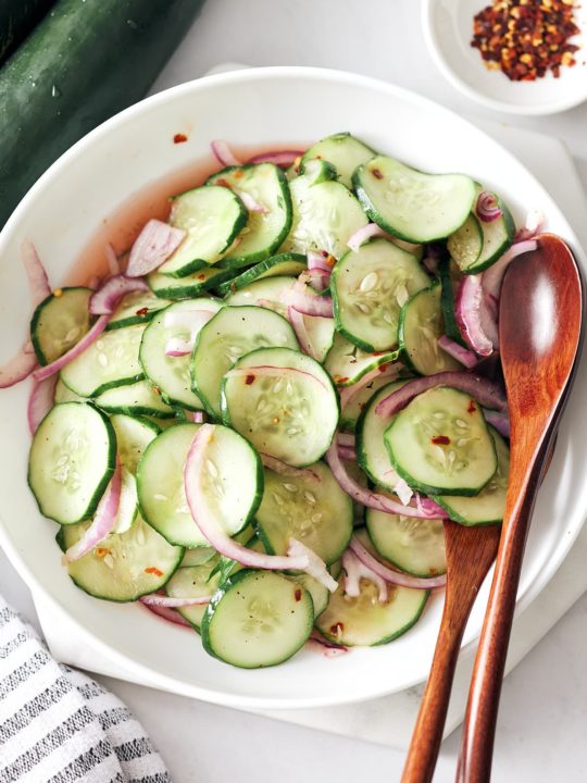 Southern cucumber salad with red onion in a bowl with wooden salad spoons.