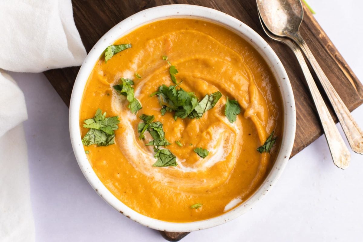 overhead of a bowl of carrot and lentil soup with cilantro garnish and two spoons