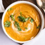 overhead of a bowl of carrot and lentil soup with cilantro garnish and two spoons