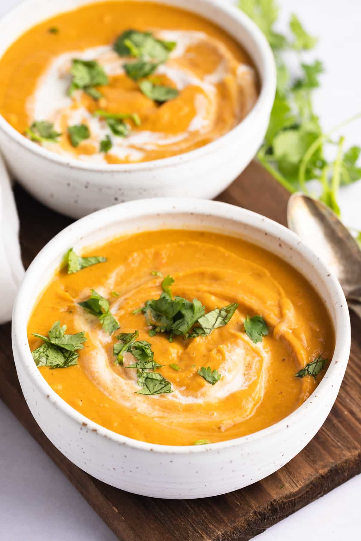 overhead of two bowl of carrot and lentil soup with cilantro garnish and two spoons