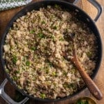 Overhead view of dirty rice with ground sausage, parsley, and the holy trinity in a black skillet with a wooden spoon