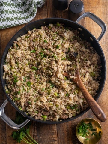 Overhead view of dirty rice with ground sausage, parsley, and the holy trinity in a black skillet with a wooden spoon