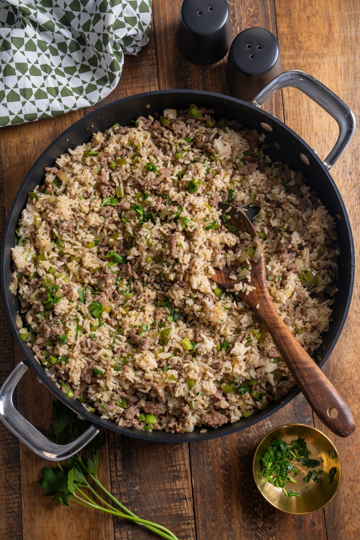 Overhead view of dirty rice with ground sausage, parsley, and the holy trinity in a black skillet with a wooden spoon