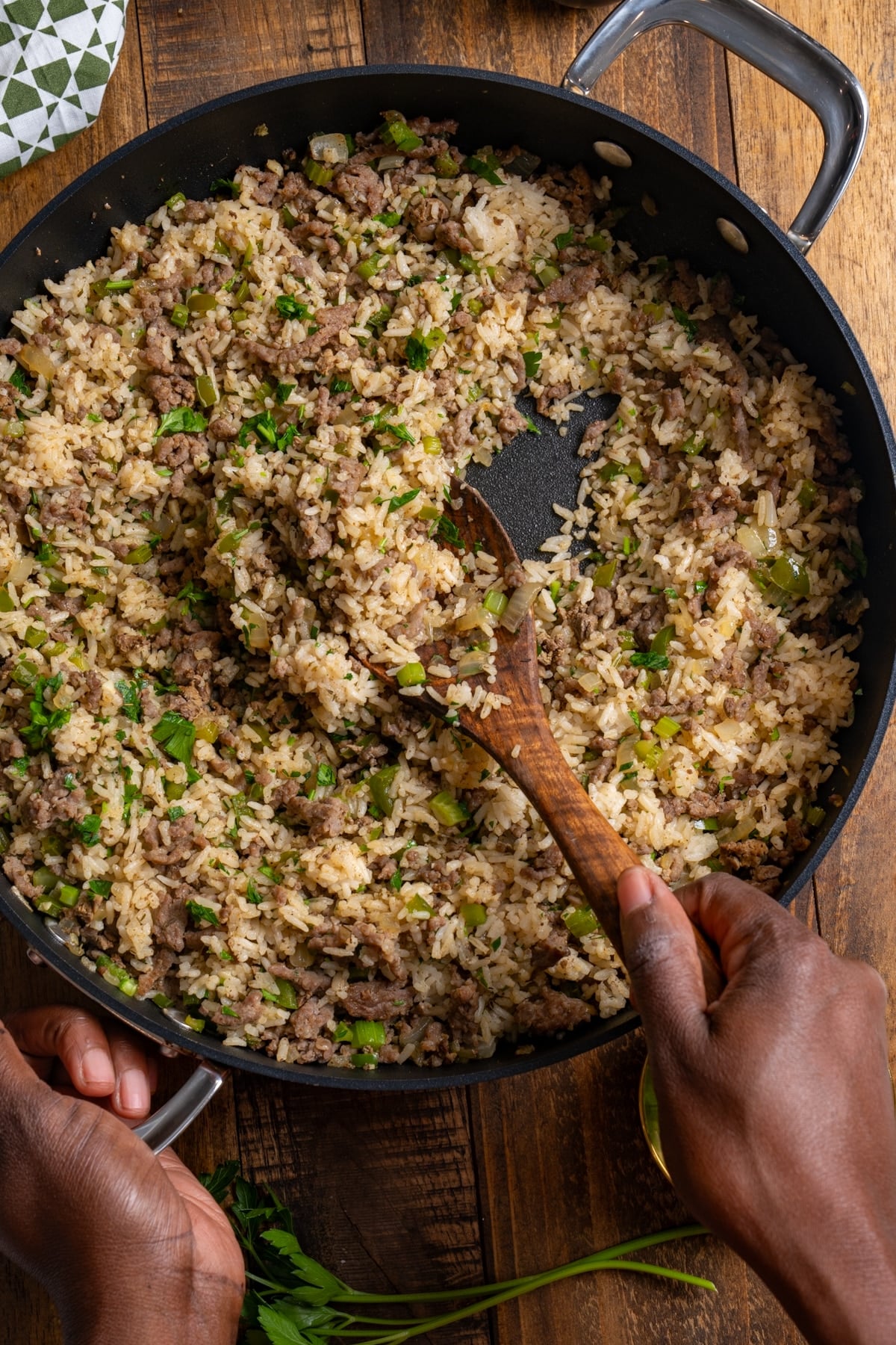 dirty rice in skillet with hands holding wooden spoon