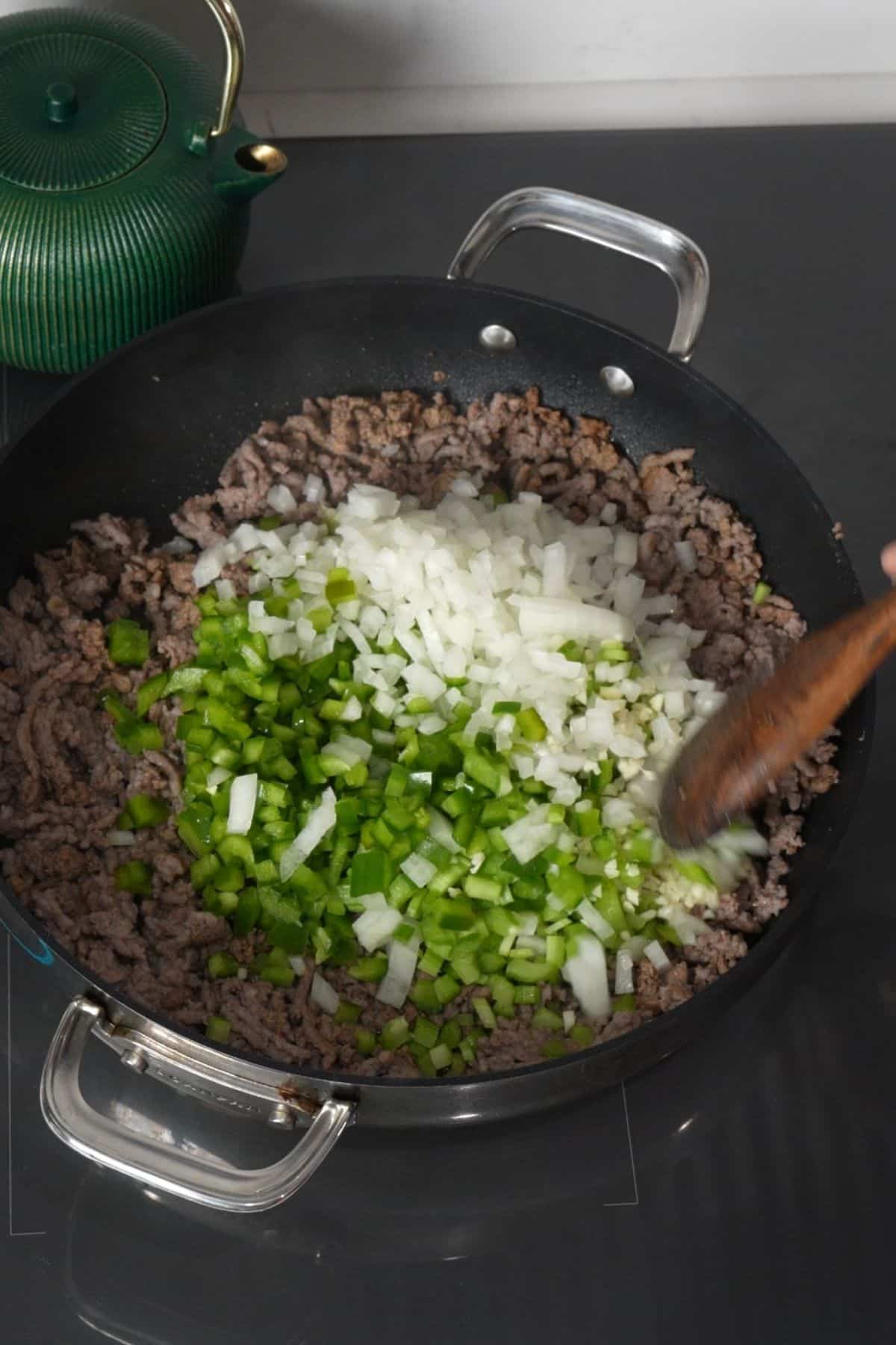 Chopped onion, celery, green bell pepper, and garlic added to browned sausage in a skillet