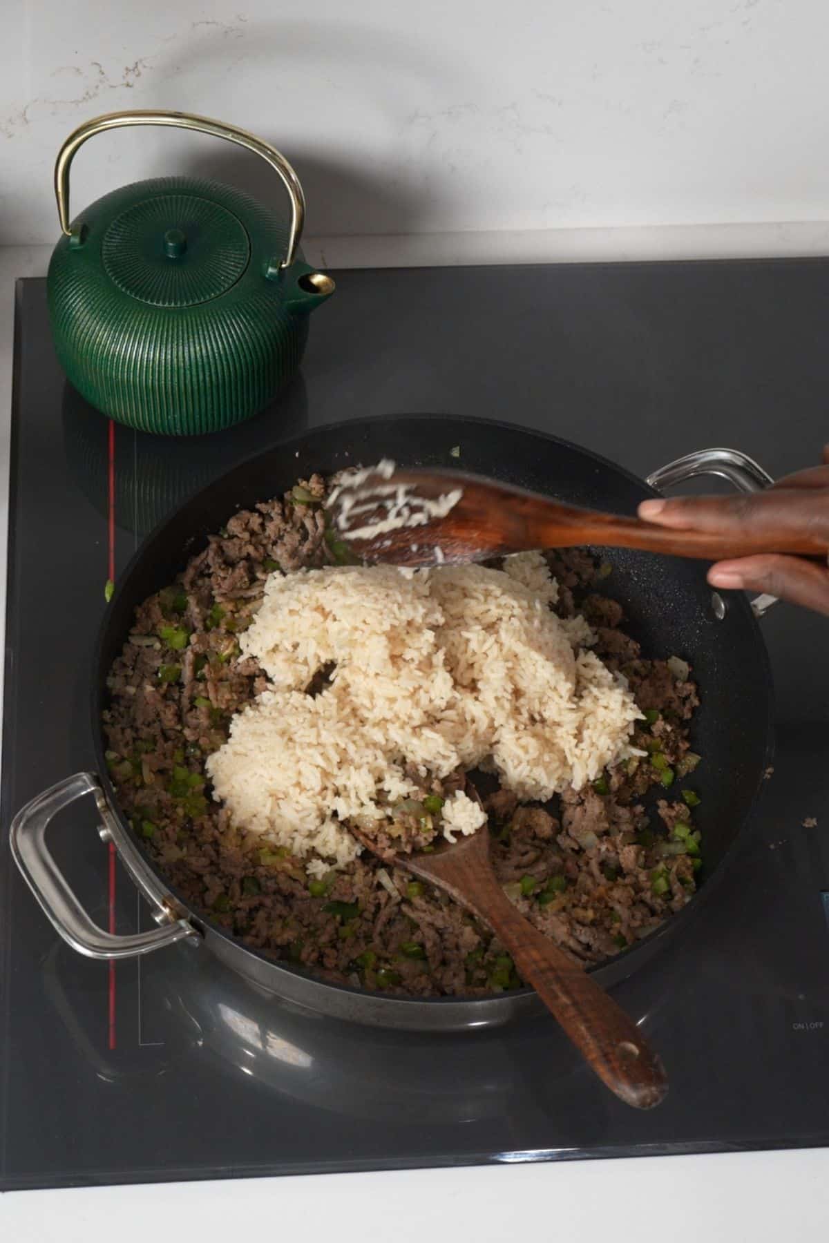 Cooked white rice being folded into seasoned sausage and vegetables in a skillet