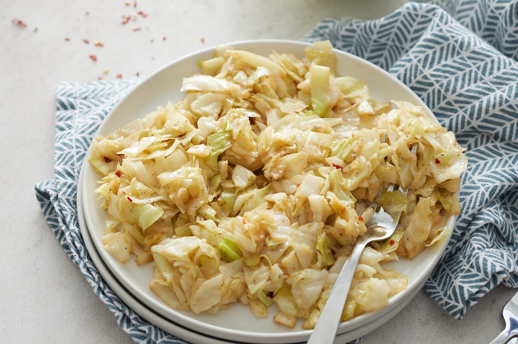 cabbage on a white plate with a fork next to a blue napkin