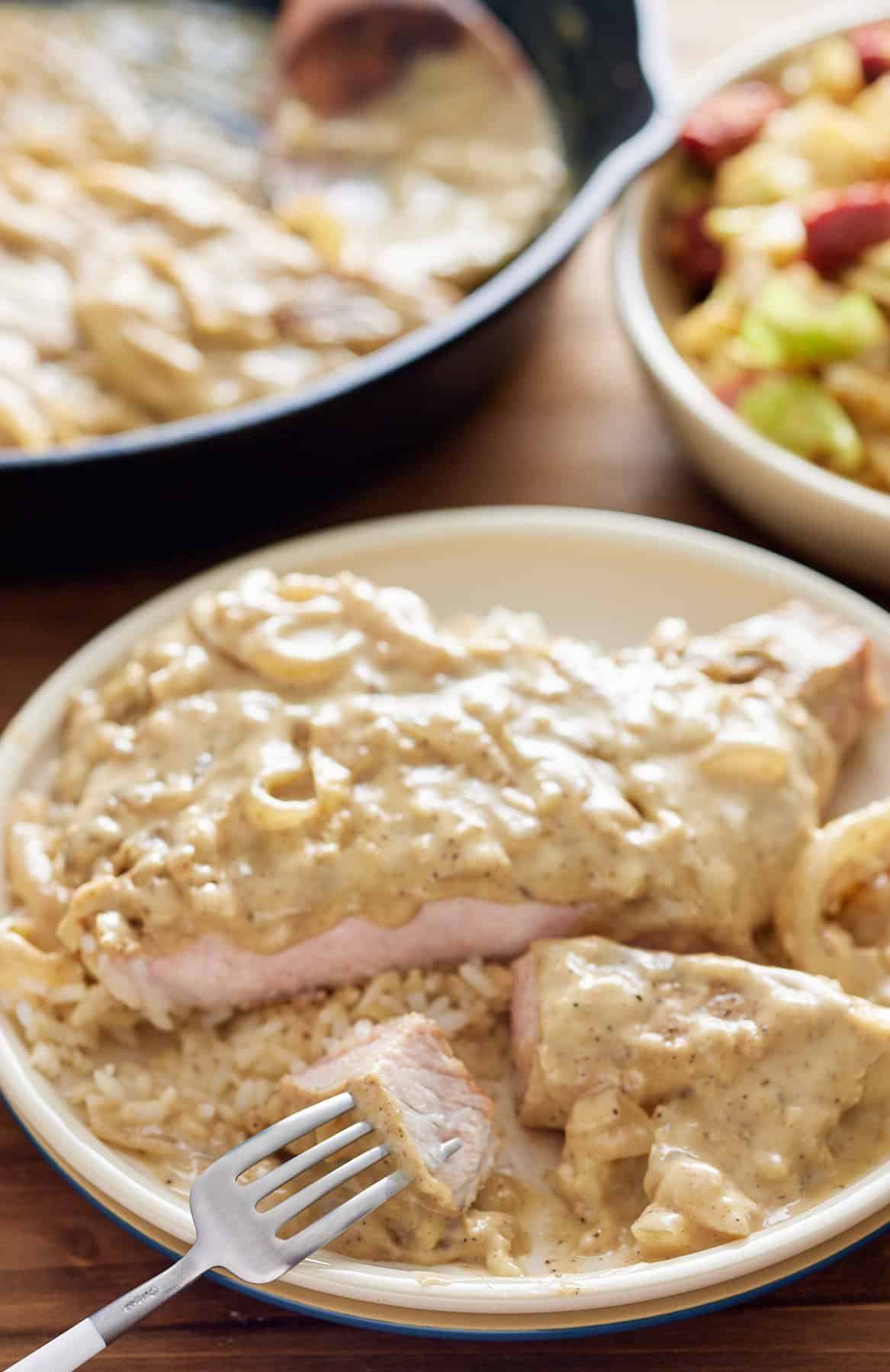 smothered pork chop on a plate with a fork and bite taken out