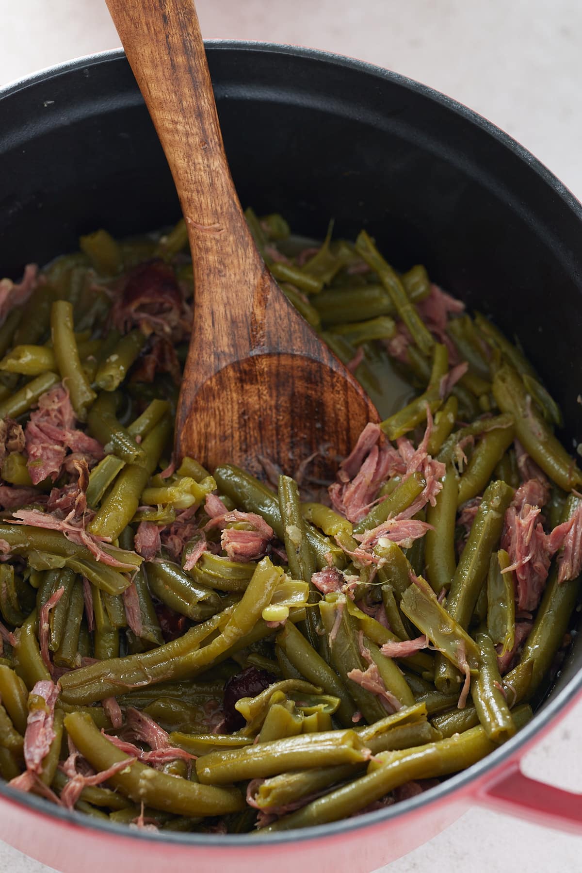pot filled with green beans and smoked turkey with a wooden spoon