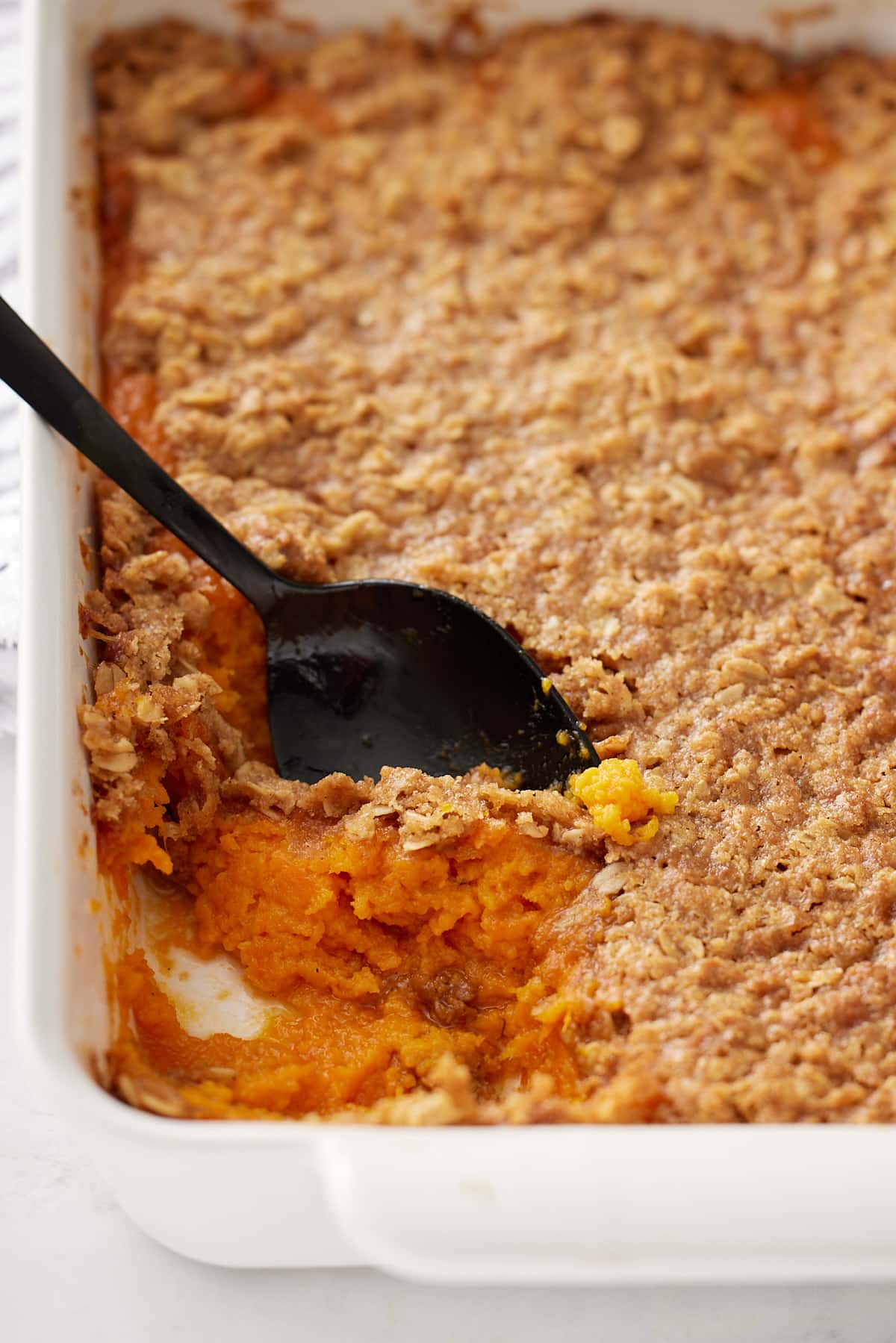 a scoop removed from the corner of the casserole dish with a spoon sticking out