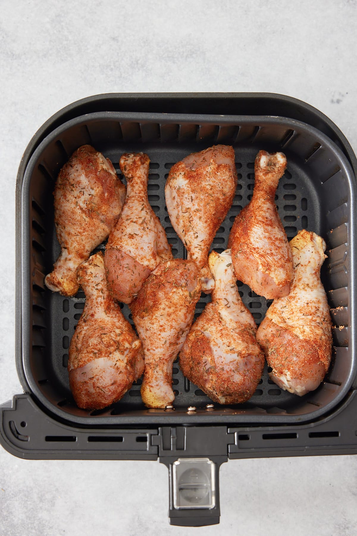 seasoned chicken drumsticks in an air fryer basket