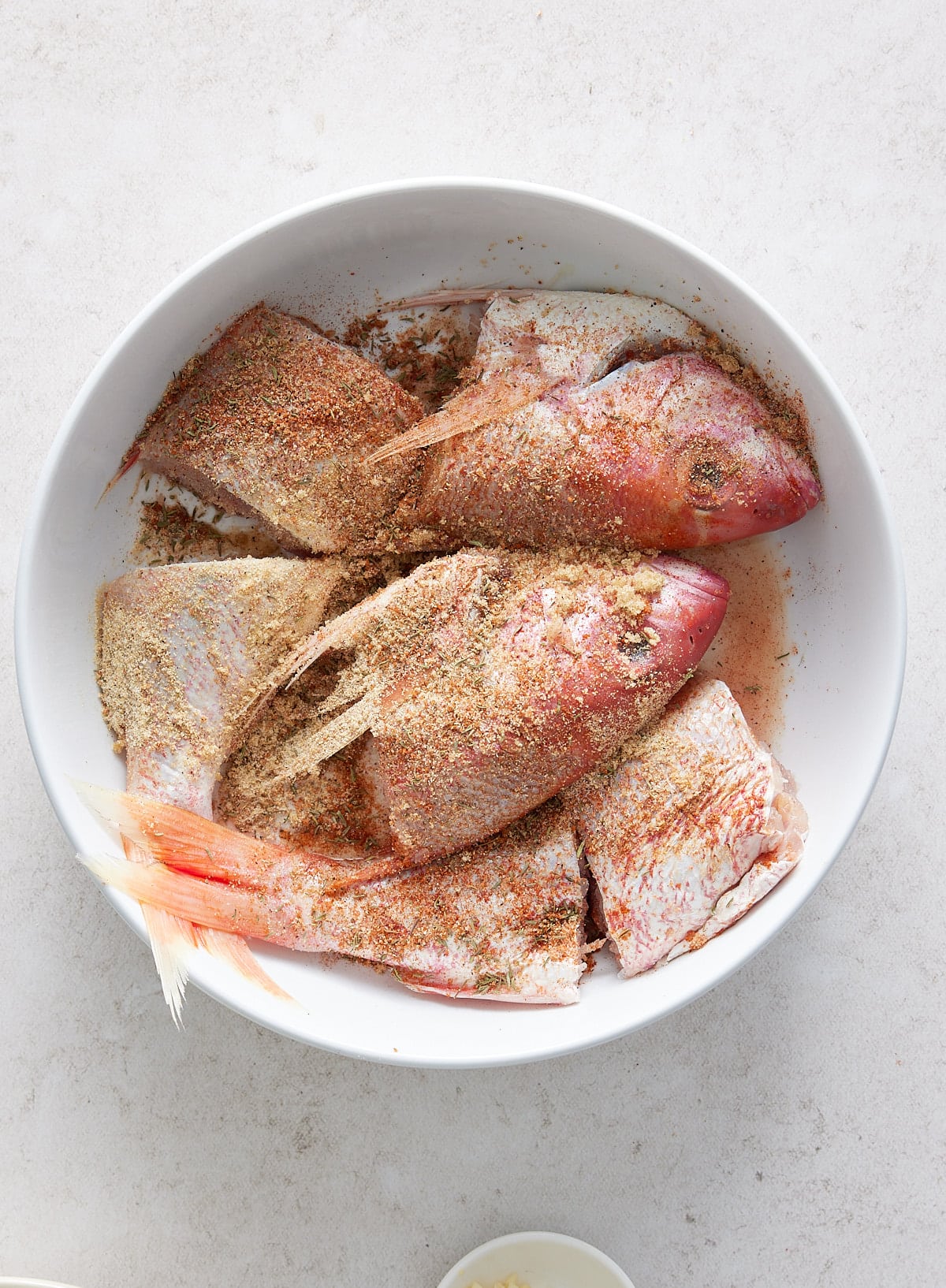 A white bowl containing spiced and seasoned snapper fillets