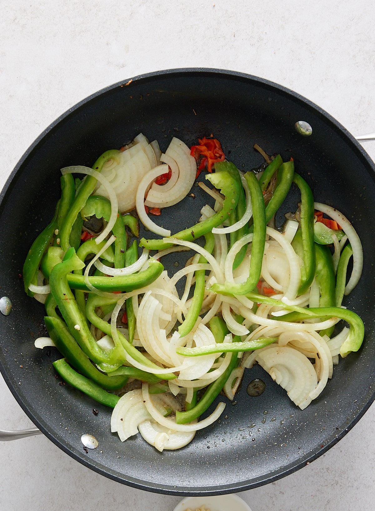 A black non-stick skillet containing sliced onion, green bell pepper and chopped red chili
