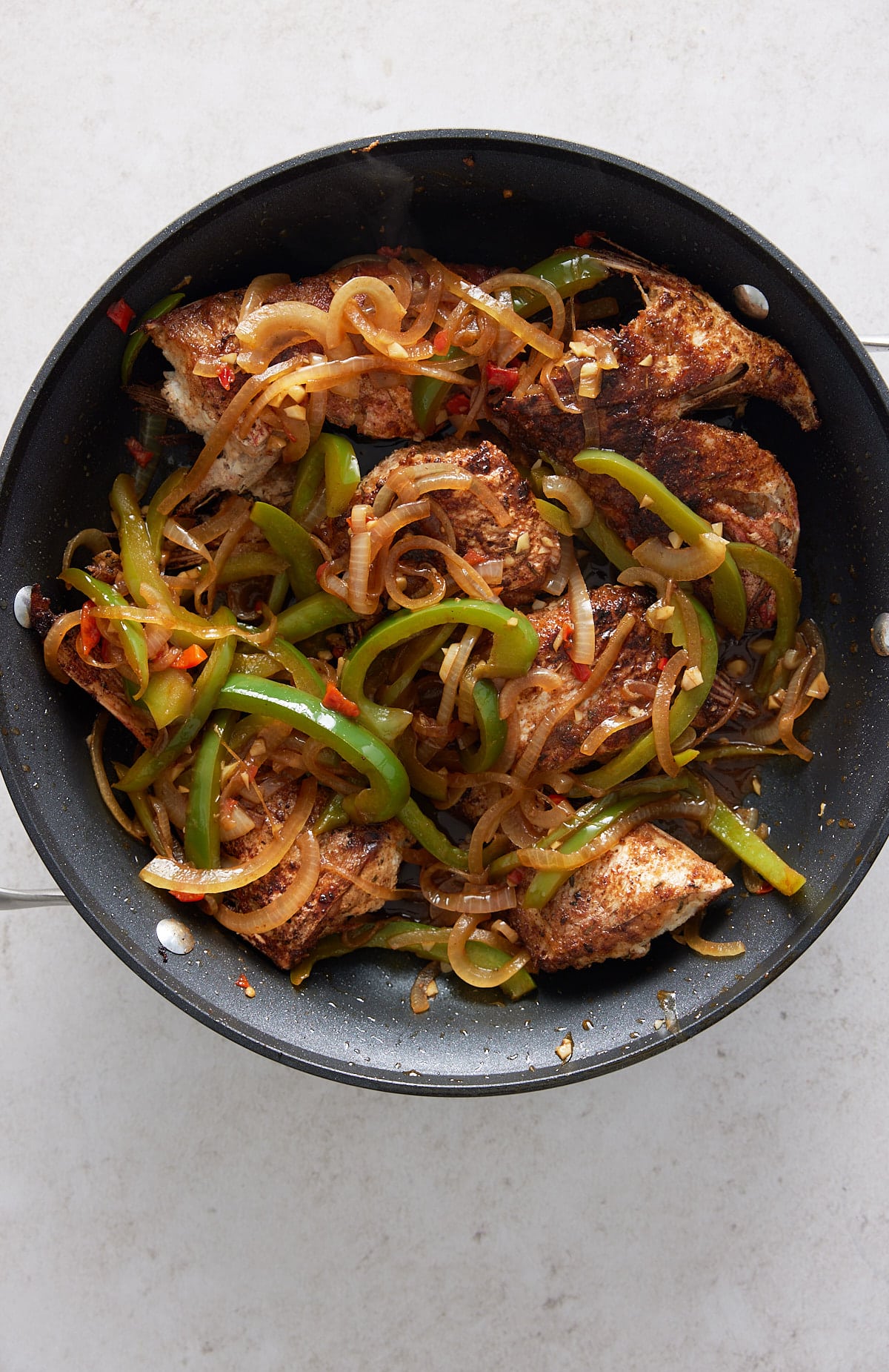 A black skillet with cooked snapper fillets and vegetables