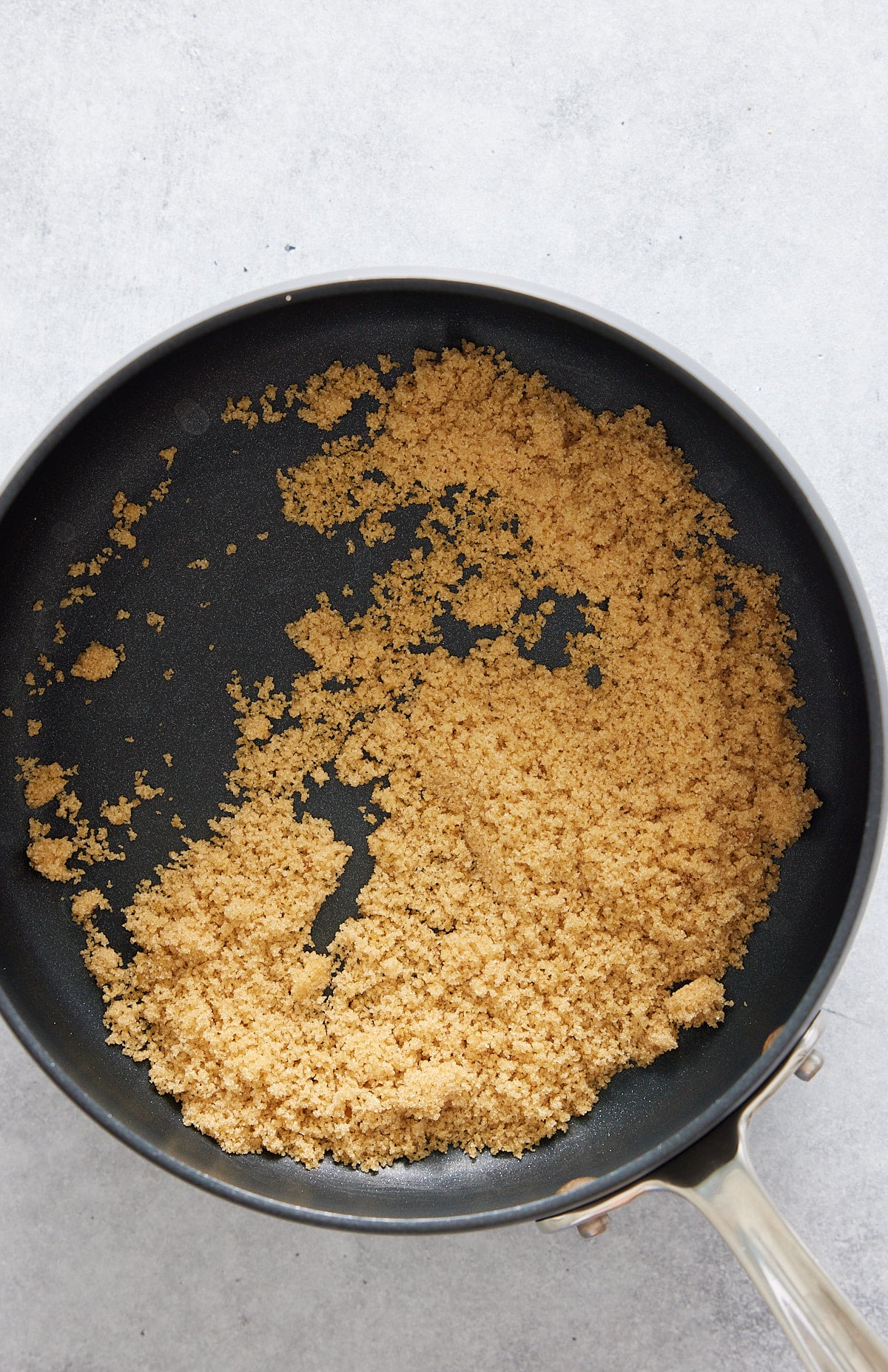 A black non-stick skillet containing brown sugar