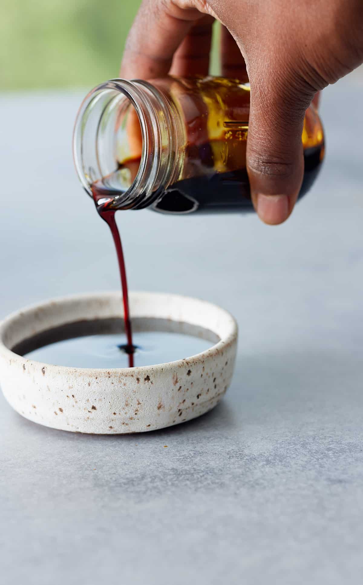 A hand holding a jar filled with browning sauce being poured into a small white bowl