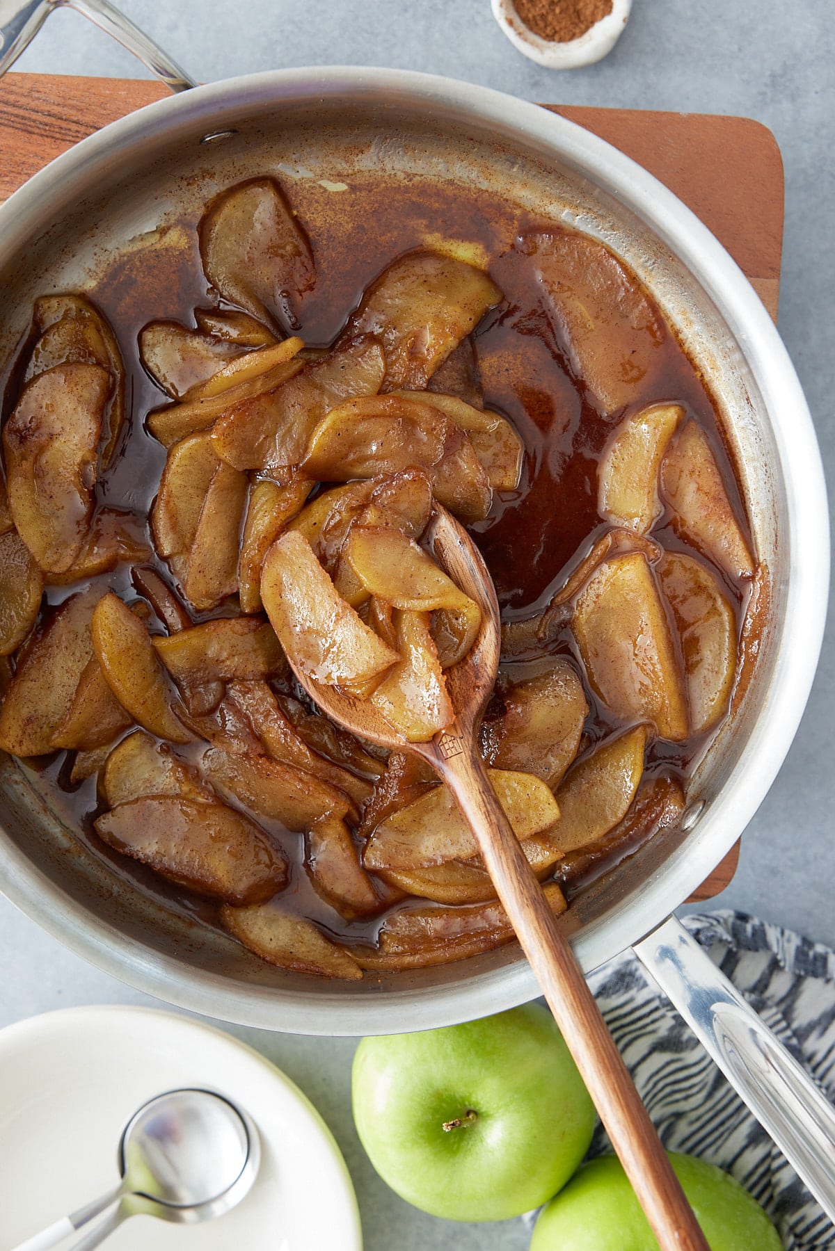 Pan with fried apples and a closeup of the apples on a wooden spoon and whole green apples set alongside