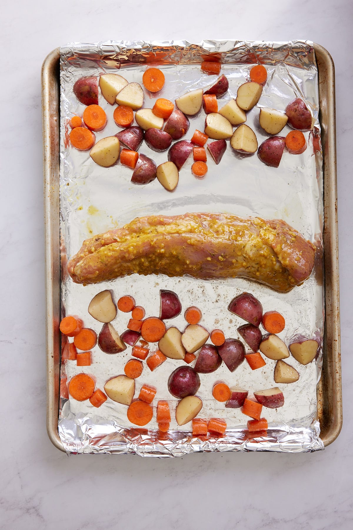 raw pork tenderloin and vegetables on sheet pan prior to baking